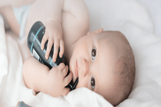  Little baby holding Manuka Biotic Eczema Relief Body Lotion bottle perfect of Nappy rash and Eczema prone skin in his hands and playing with the bottle in his mouth. 