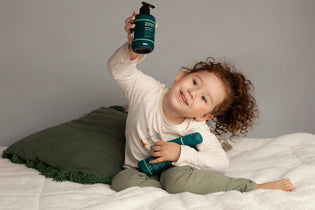  Young girl on her bed holding a bottle of Manuka Biotic Eczema Relief Body Lotion in her hand above her head and holding the Calming Body Wash in her lap for school sore impetigo natural solutions 