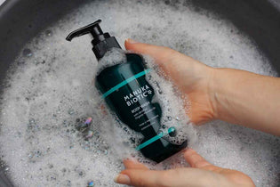  Ladies hands holding Manuka Biotic Calming Body Wash bottle in a bubble-filled wash after gently cleaning a child's skin affected by school sores and Impetigo