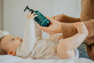  baby lying on back reaching for the Eczema Relief Body Lotion bottle being held by Mum to apply for cradle cap