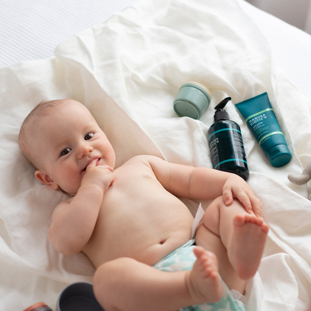  Baby smiling into the camera surrounded by bottles of Manuka Biotic products