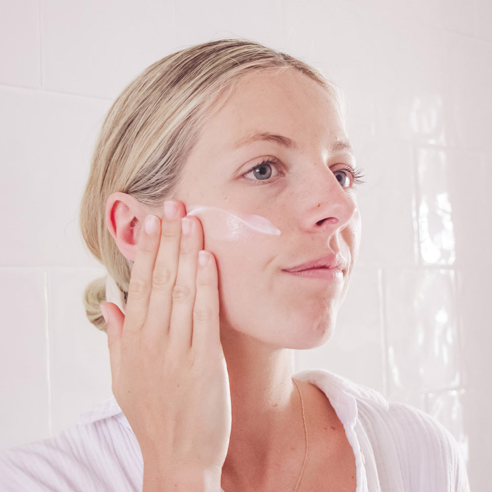  A woman putting Manuka Biotic light day cream on her cheek