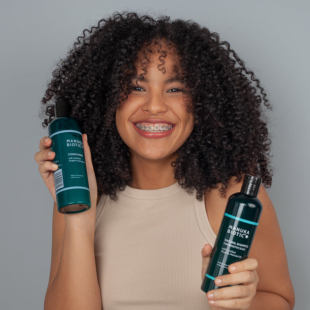  A women smiling and holding Manuka Biotic shampoo and conditioner 