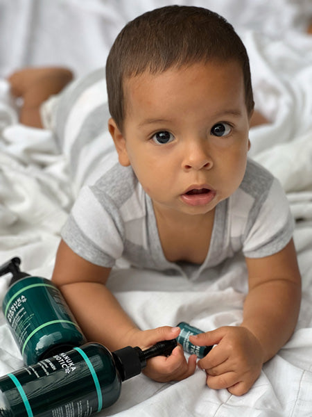  A baby looking into the camera while laying next to bottles of Manuka Biotic products 